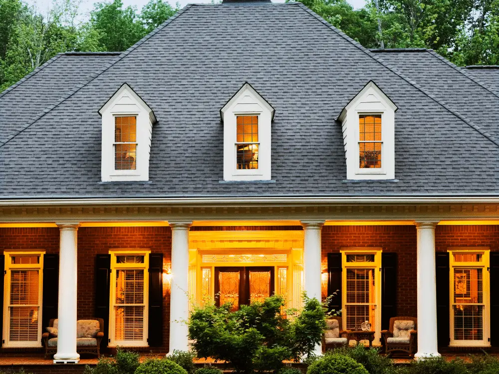Elegant home with hip-and-ridge black roof, red brick façade, and white columned front porch