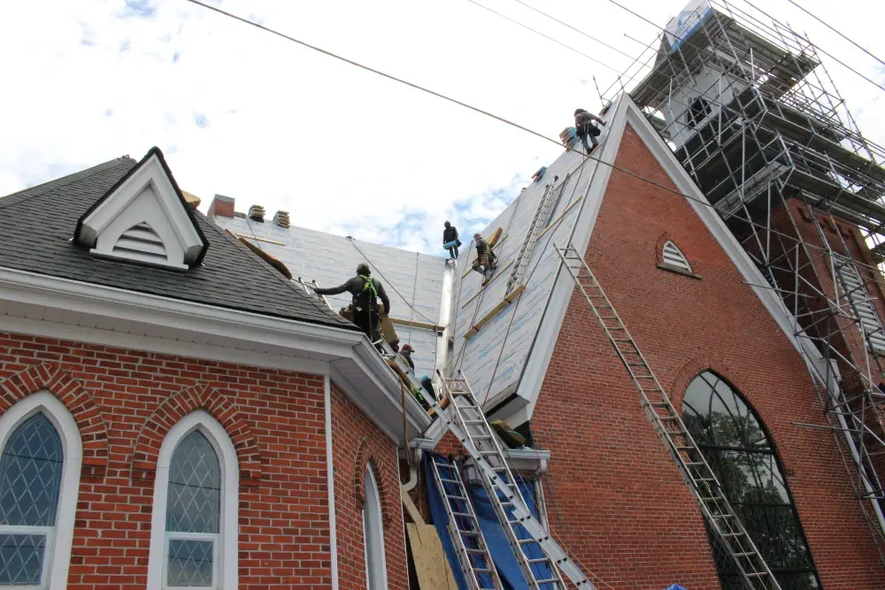 Full shot from ground of church roofing project_valley flashing_underlayment_Large roofing crew - Artisan Quality Roofing Full shot from ground of church roofing project_valley flashing_underlayment_Large roofing crew