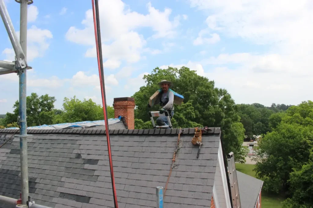 Roof crew leader at roof peak carrying shingle bundle - Artisan Quality Roofing Roof crew leader at roof peak carrying shingle bundle